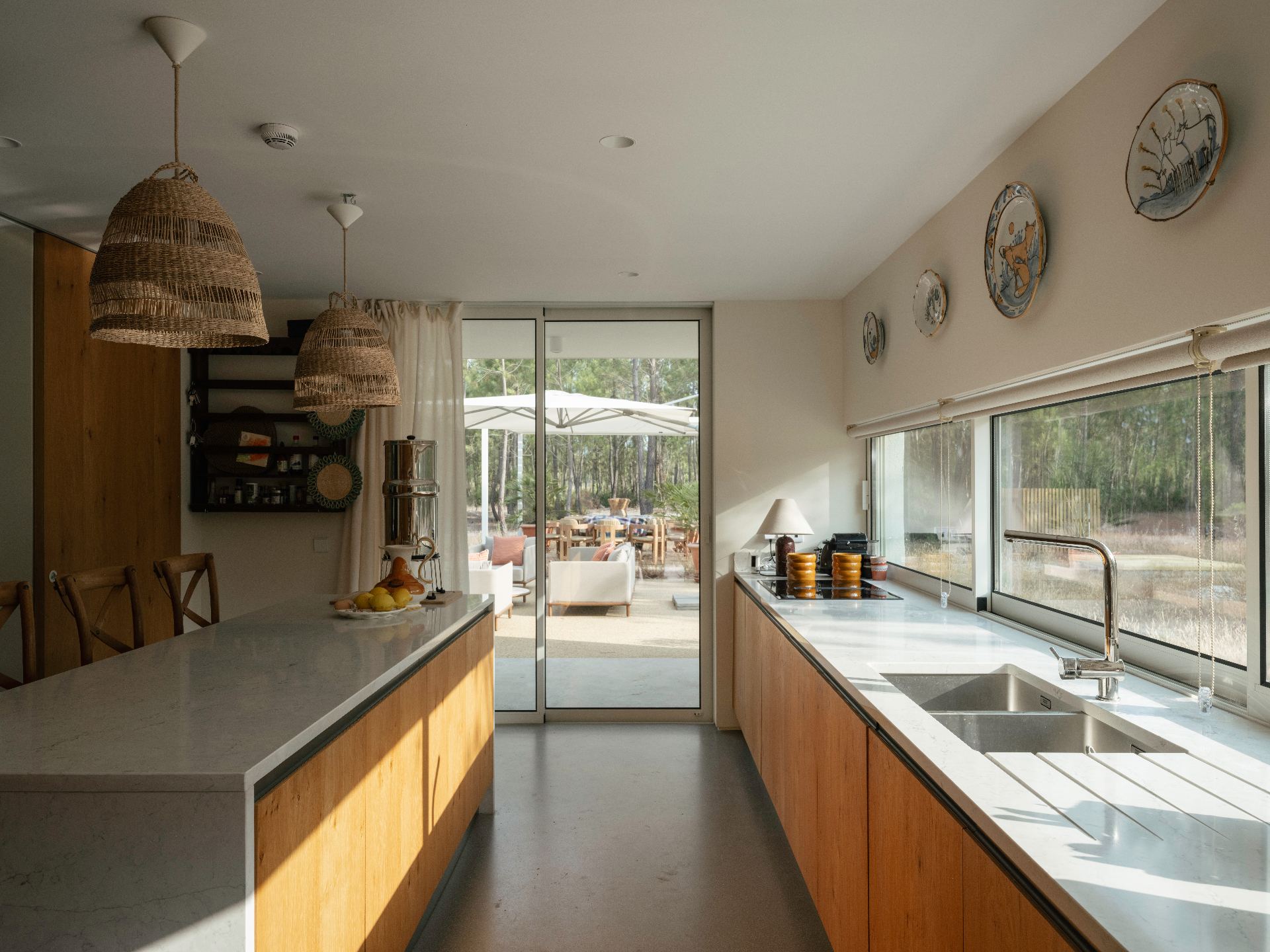 Sunlit kitchen with marble island, woven pendants, and sliding glass doors to the outdoor lounge.